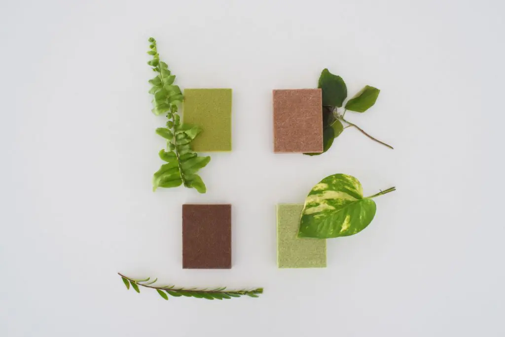 Four rectangular bars, two green and two brown PET polyester panels, are arranged on a white background with green leaves and sprigs beside each bar, suggesting a natural or eco-friendly theme.