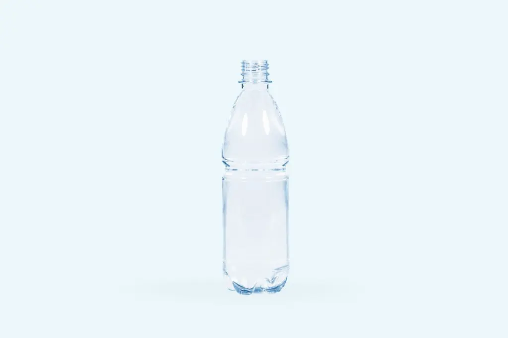 A clear plastic water bottle, filled with water and missing its cap, is standing upright against a light blue background.