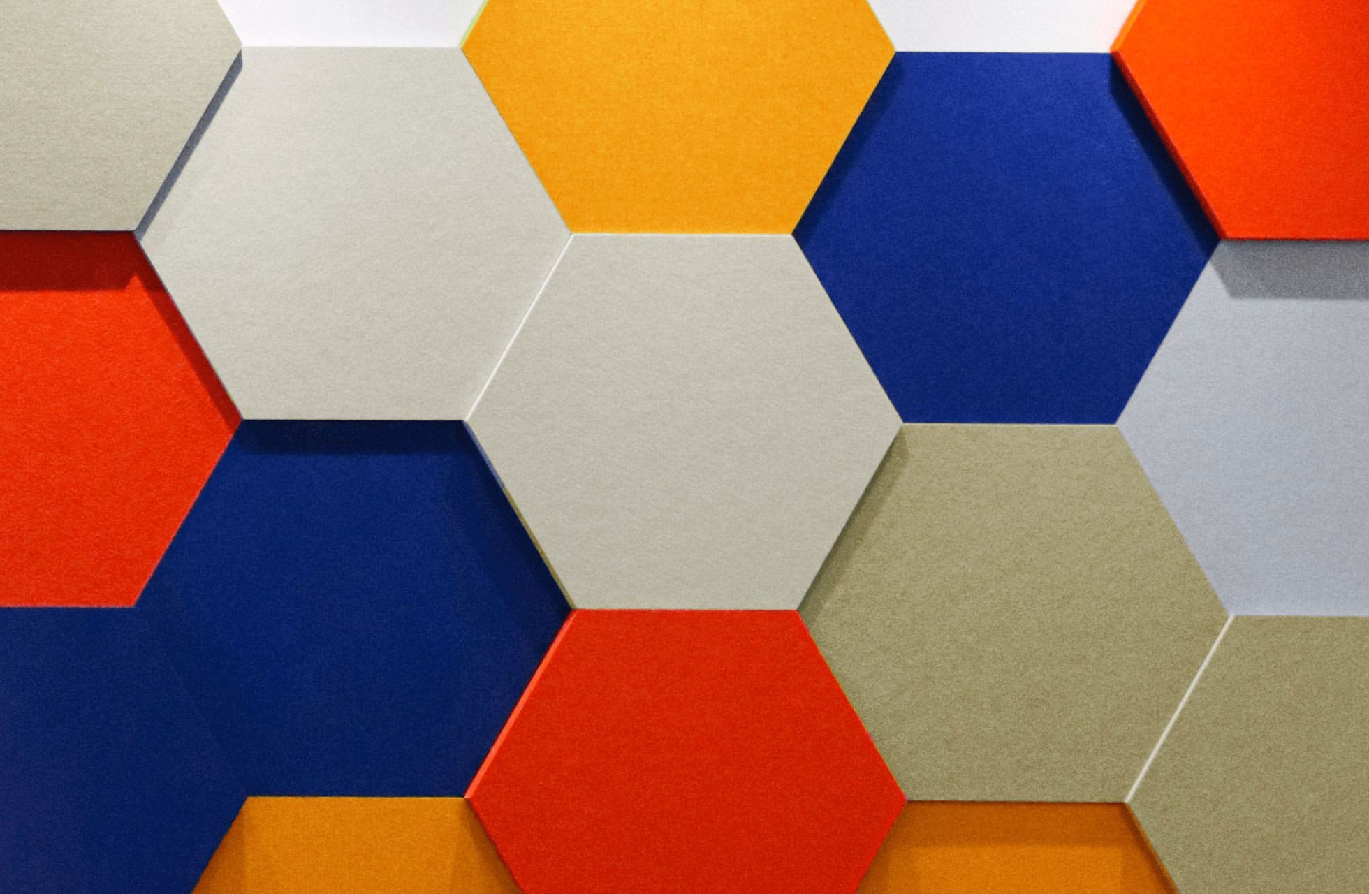A close-up of a wall decorated with hexagonal panels in red, blue, yellow, beige, and white, arranged in a geometric pattern that creates a vibrant design—ideal for soundproofing your HDB room with style.