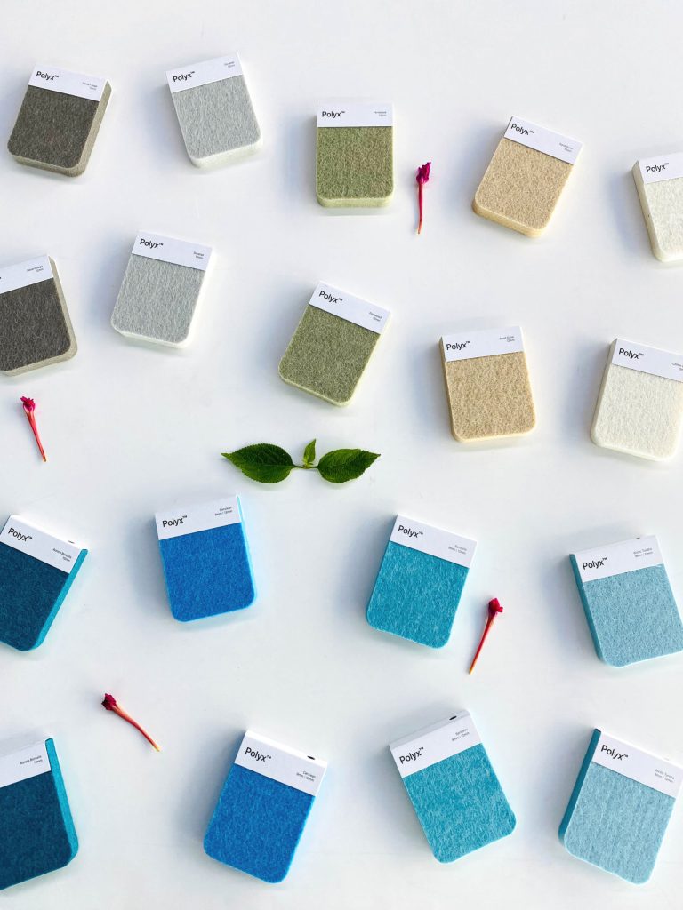 Rectangular fabric swatches in blue, gray, green, and beige are arranged on a white surface with red flower petals and three green leaves—perfect for acoustically balanced retail spaces.