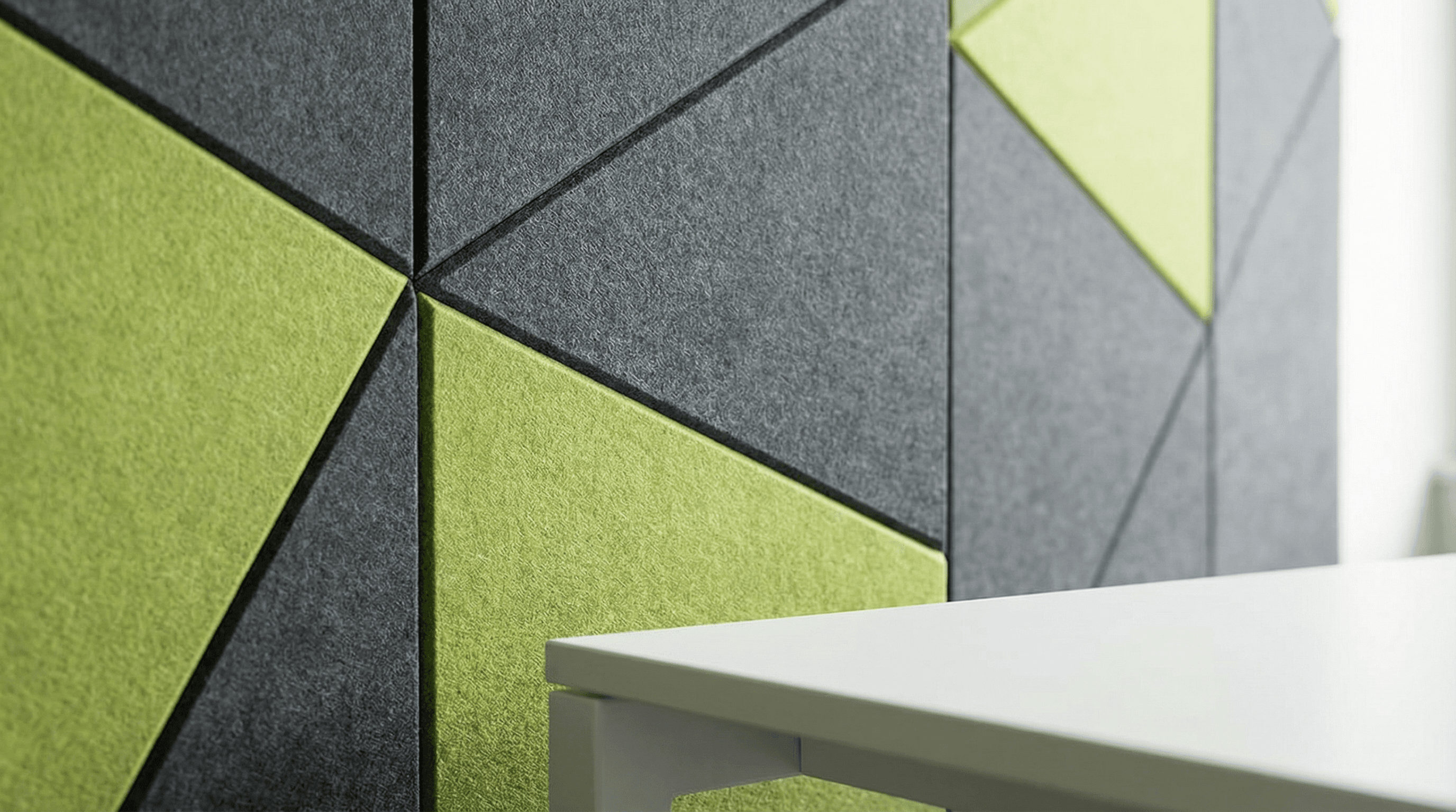 Close-up of a wall with geometric panels in gray and green, forming a modern pattern designed with AI for Acoustic Design. The edge of a white table is visible in the foreground on the right side of the image.