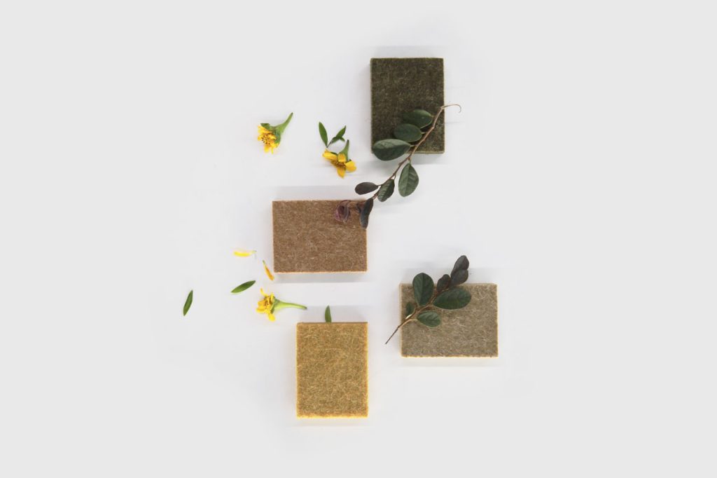 Four square FSC Chain of Custody Wall Panels in green, brown, tan, and beige are arranged on a white surface, decorated with yellow flowers and green leaves.