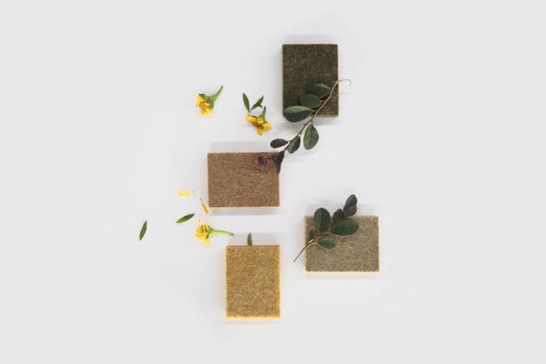 Four square FSC Chain of Custody Wall Panels in green, brown, tan, and beige are arranged on a white surface, decorated with yellow flowers and green leaves.