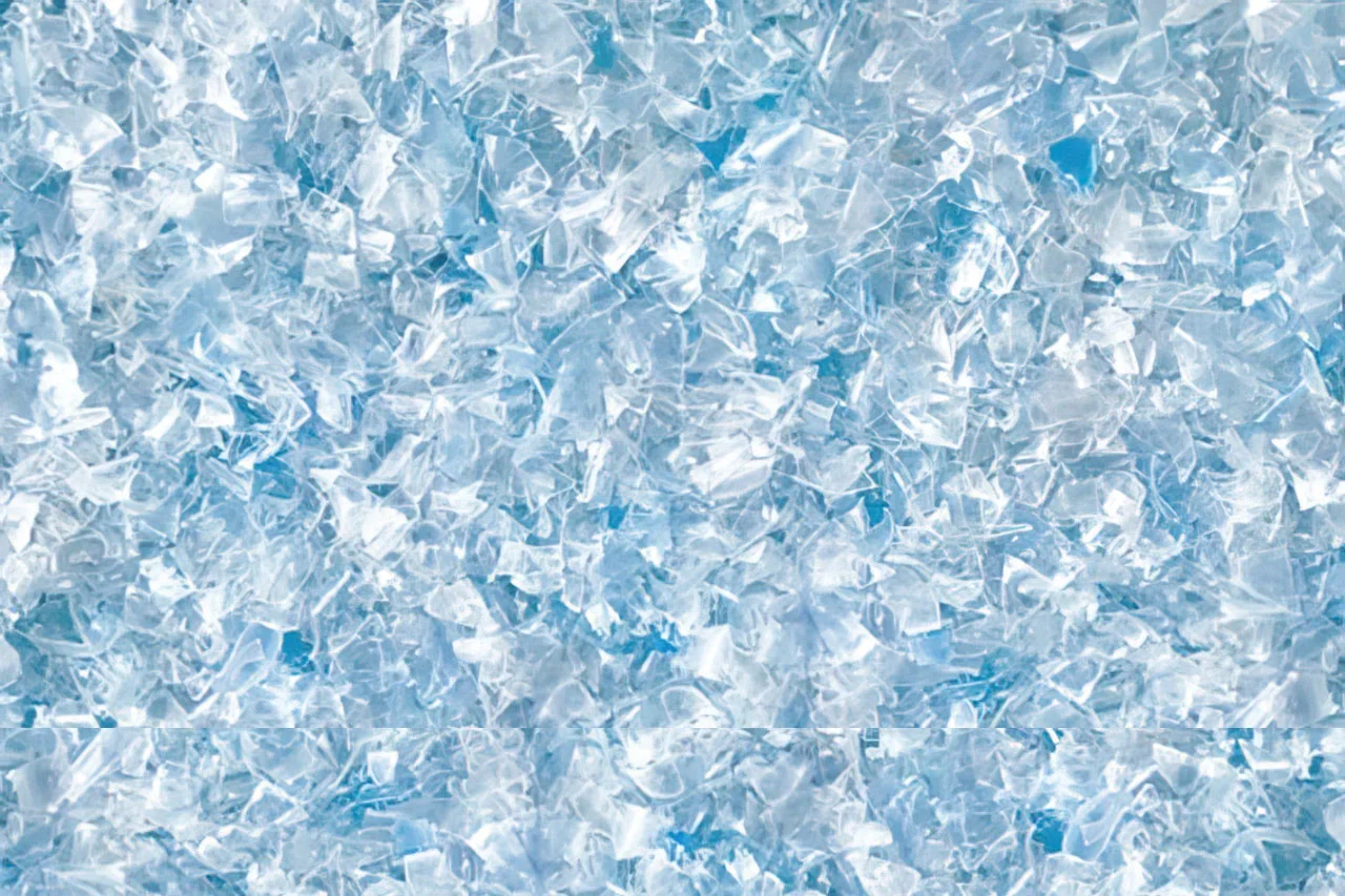 Close-up of many small, translucent, blue-tinted plastic flakes or chips scattered closely together, creating a textured, crystalline appearance.