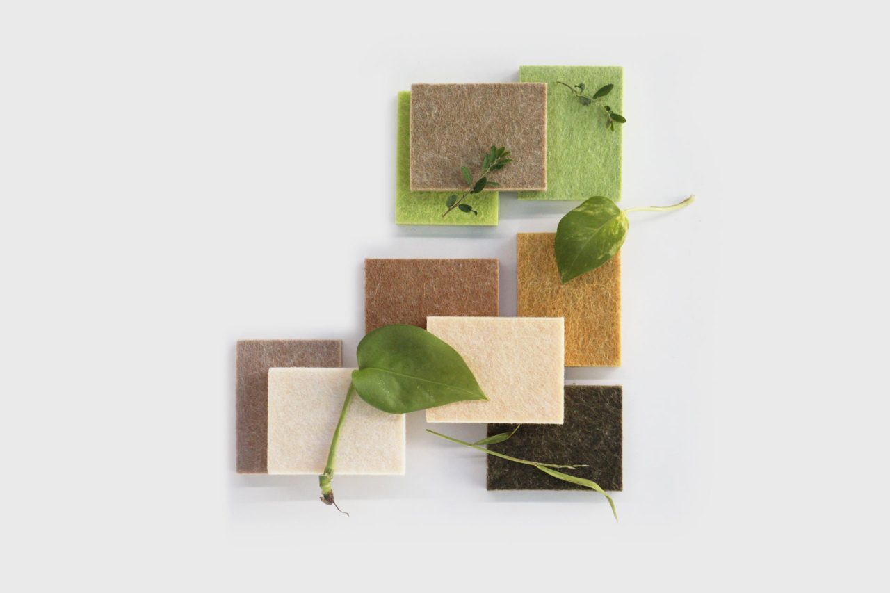 Rectangular felt fabric swatches in earthy tones—green, brown, beige, and tan—are arranged in a grid pattern alongside green leaves and small plant stems, showcasing the natural aesthetic of PET polyester panels.