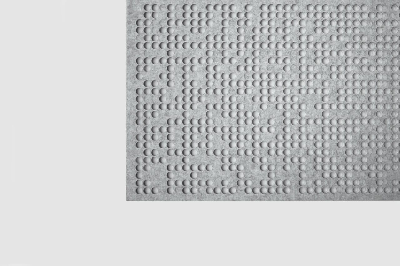 A close-up of a white surface with raised dots arranged in patterns, representing text in Braille, positioned in the upper right corner on a plain light background, highlighting our Polyester Acoustic Panels Offerings.
