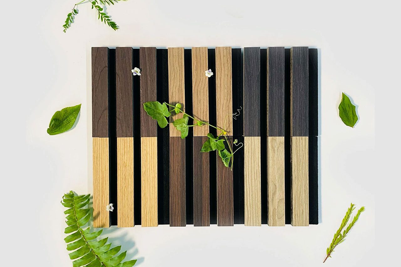 A rectangular wooden tray with alternating light and dark vertical slats, decorated with small white flowers and green vines, is surrounded by assorted green leaves and ferns on a white background. Explore Our Other Acoustical Products to complement your decor.