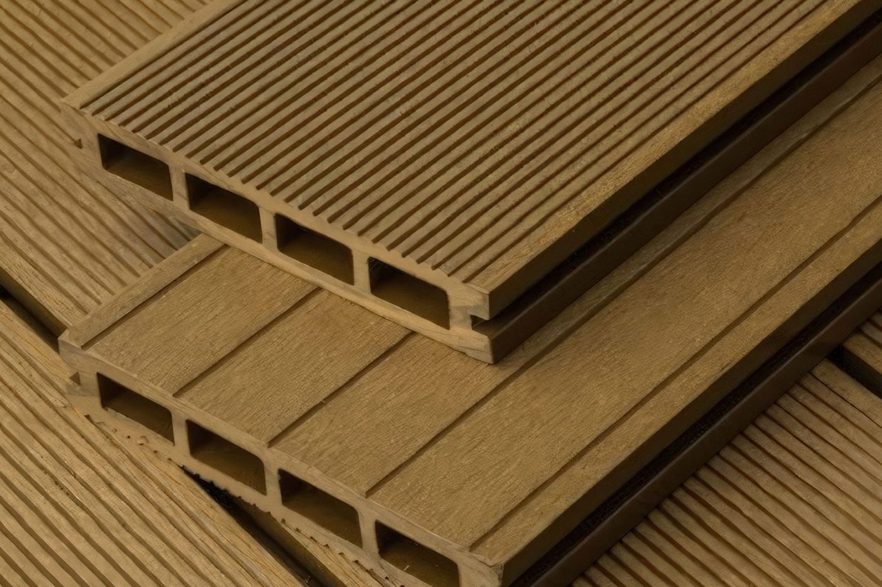Close-up of stacked, rectangular composite decking boards with hollow centers and grooved surfaces. The boards have a wood-like texture and are arranged on a matching grooved deck, complementing Our Other Acoustical Products for cohesive design solutions.