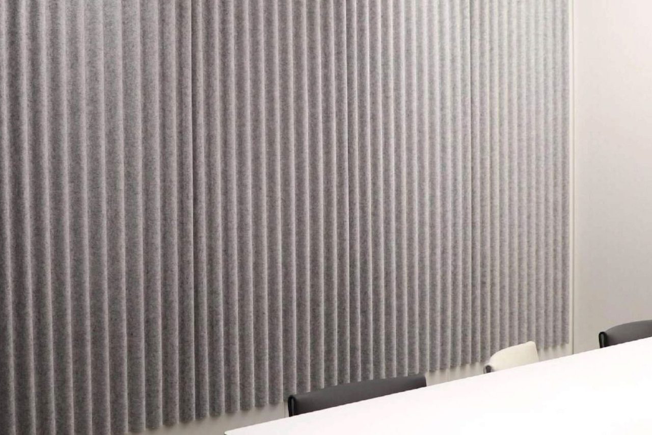A conference room features a white table with several dark and light-colored chairs. The wall is lined with vertical Polyx Curved Acoustic Panels designed to absorb sound.