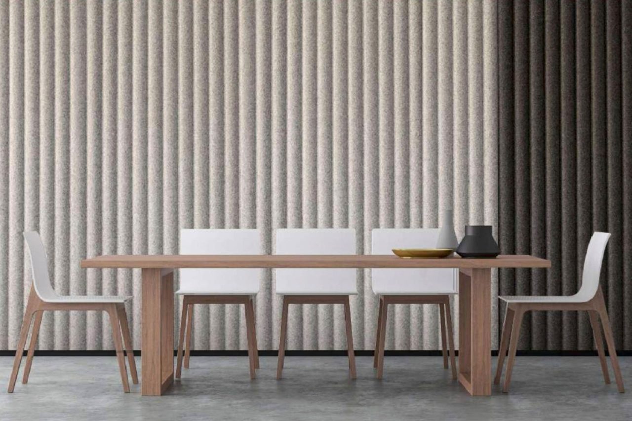A modern dining room with a wooden table, five white chairs, and minimalist decor. The background features textured Polyx Curved Acoustic Panels with vertical gray sections in varying shades.